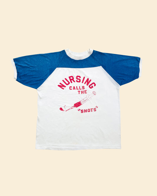 Blue and white t-shirt with 'Nursing calls the shots' text on a beige background